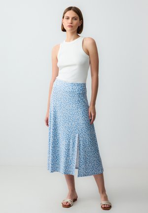 Blauer Blumenkleid mit einem seitlichen Schlitz, aus leichtem Material gefertigt. Kombiniert mit einem weißen ärmellosen Top. Die Sandalen haben ein breites Riemendesign.