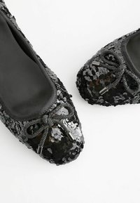 Mustat paljettiballerinat, joissa on pyöreä kärki, pehmeä sisävuori ja koristeellinen nauha metallisine yksityiskohtineen edessä.