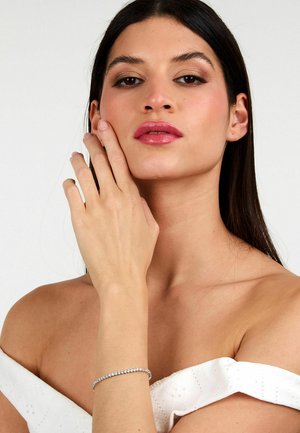 Bracciale d'argento con cristalli trasparenti e rotondi, indossato su un polso marrone chiaro. Il modello ha i capelli lisci e scuri ed indossa una maglietta bianca senza spalline.