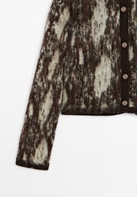 Cardigan marron et crème duveteux à manches longues avec cinq boutons métalliques sur une bordure verticale foncée à l'avant.