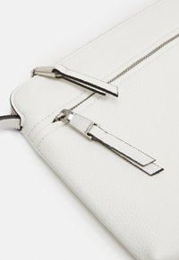 Pochette en cuir blanc avec une finition texturée, quincaillerie en argent, double tirette de fermeture éclair et surpiqûres contrastantes le long des bords.