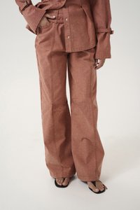 Rust-colored wide-leg trousers with a textured fabric. Features visible stitching, front pockets, and a relaxed fit.