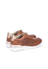 Zapatillas de cuero marrón con un patrón floral cortado a láser, suela blanca y acentos metálicos dorados en el talón y los cordones.