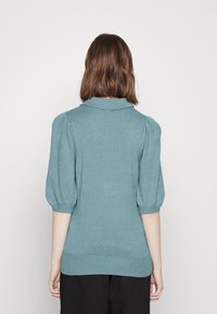 Tyrkysový pletený svetr s límcem, krátkými nabíranými rukávy a žebrovaným lemem. Hladká struktura a přiléhavý silueta, zdůrazňující design na zadní straně.