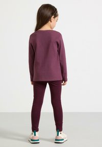 Langærmet lilla top med ribbet tekstur kombineret med matchende lilla leggings. Skoene har en hvid base med grønne og rosa accenter.