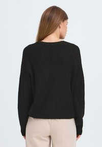 Pull noir côtelé avec un large col et des manches longues, présentant une coupe décontractée et un motif tricoté texturé.