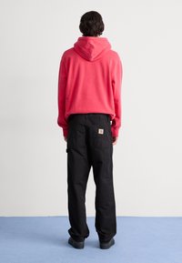Felpa rossa con cappuccio e vestibilità rilassata, abbinata a pantaloni cargo neri con più tasche. Calzature nere completano l'outfit.