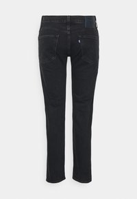 Jeans de mezclilla negra con un corte recto. Sus características incluyen cinco bolsillos, un parche de cuero en la parte posterior y un detalle de costura mínima.