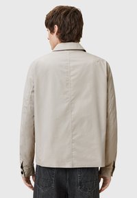 Lichtbeige jasje met een kraag, knopenmanchetten en een split aan de achterzijde. Zachte textuur, getailleerde pasvorm en een schoon ontwerp zonder versieringen.