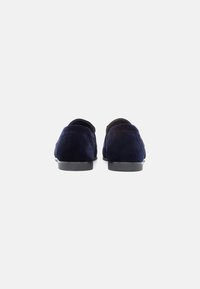 Loaferi din suede bleumarin cu o talpă joasă din cauciuc negru, vârf rotunjit și detalii discrete de coasere în spate. Textură netedă și design minimalist.