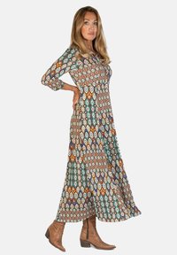 Długa, wzorzysta sukienka z geometrycznym wzorem w kolorach ziemi. Wykonana z lekkiego materiału, z rękawami o długości trzech czwartek i luźnym krojem.