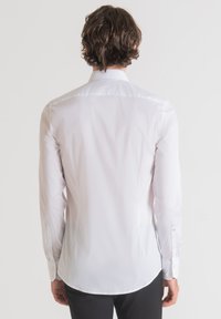 Camicia bianca a maniche lunghe con colletto classico, polsini abbottonati e un tessuto liscio e texturizzato con una vestibilità sartoriale.