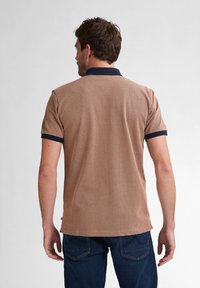 Brun kortärmad polo med en strukturerad mönster och marinblå krage och manschetter. Har en lätt svans i nederkant och sidofickor.