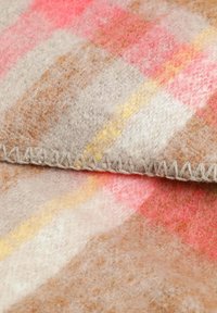 Vlněná deka s jemnou texturou v odstínech béžové, růžové a žluté se vzorem káro a prošívaným okrajem.