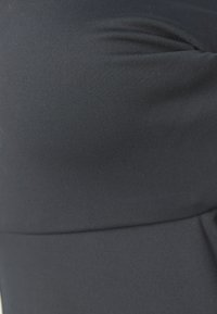 Nærbilde av et svart, elastisk stoff med en glatt tekstur, som har subtil ribbing og en samlet sømdetalj.