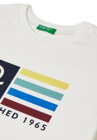 Bílé bavlněné tričko s kulatým výstřihem. Má grafický motiv s výraznými horizontálními pruhy ve žluté, tyrkysové, modré a vínové barvě.