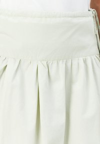 Lys grøn nederdel med plisseret design, lavet af letvægtsmateriale. Har en rynket talje og snore i siderne.