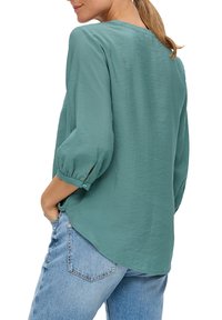 Turquoise, lichtgewicht blouse met driekwart mouwen en een afgeronde zoom. Geweven stof, plooi-detail op de mouwen en knopen bij de manchetten.