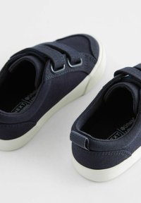 Marine kanvas sko med to velcro-remme, hvide gummisåler og afrundede tæer. Har minimal syning og en trækflig ved hælen.