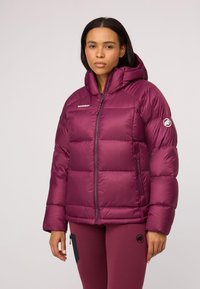 Fioletowa kurtka puchowa z zapięciem na zamek błyskawiczny i kapturem. Posiada pikowany wzór, logo na klatce piersiowej oraz boczne kieszenie. Gładki, błyszczący materiał.