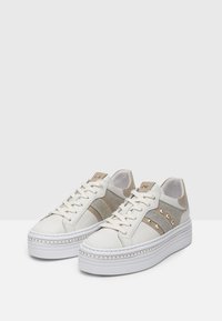 Sneakers bianchi in pelle con accenti di glitter beige e borchie dorate. Suola piatta bianca spessa con cuciture decorative. Chiusura con lacci.
