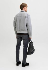 Gray wool-blend bomber jacket with ribbed cuffs, high collar, and side pockets, paired with dark denim jeans and a black tote bag.