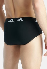 Svarta simbyxor med en slät yta och elastisk midja, som har ett vitt tre-stripes design på baksidan.