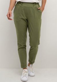 Olive green trousers with a soft texture, tapered fit, elastic waistband, and front pockets. Cuffed hems complement casual white sneakers.
