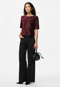 Bordo blizgučių palaidinė su trumpomis rankovėmis, derinama su juodomis, didelėmis kelnėms su aukštu liemeniu. Aksesuarai apima mažą juodą rankinę.