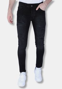 Zwarte distressed jeans met een slim fit, voorzien van meerdere gescheurde accenten, een klassieke vijf-pocket ontwerp en een knoopsluiting. Gepaarde met witte sneakers.