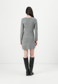 Robe grise à manches longues avec une silhouette ajustée, fabriquée en tissu doux, associée à des bottes en cuir noir montantes avec des talons épais.