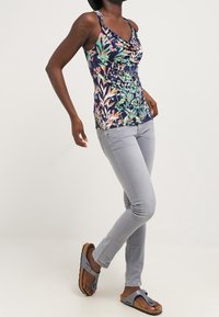 Floral sleeveless top with cowl neck, featuring blue, green, and pink colors. Paired with light gray skinny jeans and gray sandals.