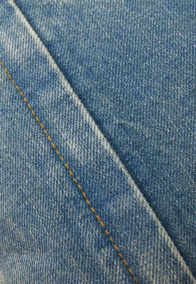 Heled sinine denimkangas, millel on tekstureeritud kude. Nurga all seamide ääres on kollased õmblused, mis loovad silmatorkava kontrasti.