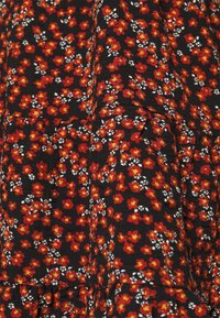 Tessuto nero con un motivo floreale che presenta fiori rossi e bianchi. La texture appare morbida con pieghe arricciate all'orlo.