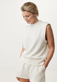 Ärmelloses weißes Top aus weichem Stoff, mit hohem Kragen und entspanntem Schnitt, kombiniert mit passenden Shorts, minimalistischem Design.