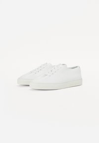 Baskets blanches en cuir texturé, arborant un design minimaliste avec des semelles en caoutchouc beige et six œillets pour les lacets.
