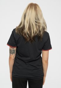 Black t-shirt with red accent on sleeves, short sleeve design, soft texture, simple cut, and noticeable tattoo on the left arm.