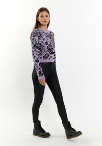Liliowa dziergana sweter z czarnymi wzorami paisley, okrągłym dekoltem i długimi rękawami, zestawiony z czarnymi dopasowanymi spodniami i czarnymi sznurowanymi botkami.