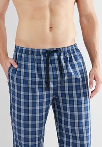 Blauwe en witte geruite pyjamabroek met een elastische tailleband, een knoop aan de voorkant en een zwarte trekkoord, gemaakt van lichtgewicht stof.