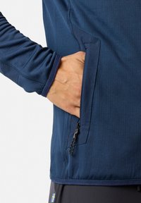 Marineblauw langärmige shirt met contrasterende stiksels en een externe zak met rits. Glad, ademend stof met een aangesloten ontwerp.