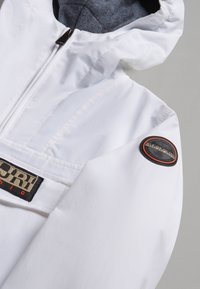 Veste blanche résistante aux intempéries avec fermeture éclair, intérieure grise et patch logo sur la manche. Présente des détails cousus et une capuche.