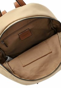 Beige Rucksack, geöffnet, um das braune Innenfutter, die Reißverschlusstasche und das gepolsterte Fach zu zeigen, mit braunem Lederreißverschluss und Akzenten.