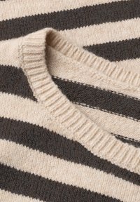 Gros plan d’un pull tricoté avec de larges rayures horizontales beige et gris foncé et un col rond côtelé.