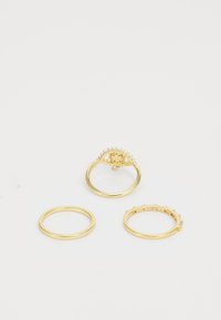Ensemble de trois bagues en or : l'une présente un design oculaire décoratif avec des pierres serties sur griffes, les autres sont simples avec des bandes lisses.