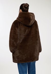 Cappotto in pelliccia sintetica marrone con un ampio cappuccio, caratterizzato da una vestibilità larga e una consistenza morbida. Il cappotto ha maniche lunghe e un orlo dritto.