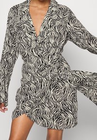 Zebra-muster Wickelkleid aus leichtem Stoff. Verfügt über einen tiefen V-Ausschnitt, lange Ärmel und eine taillierte Taille für eine figurbetonte Silhouette.