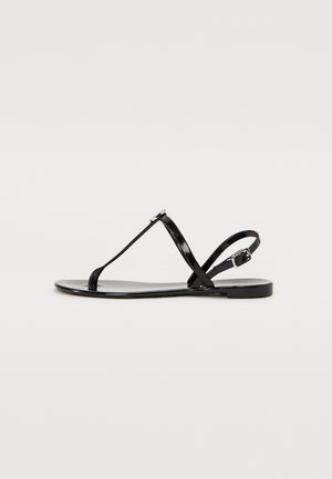 Sandálias planas pretas com um acabamento brilhante em verniz, tiras finas e fecho lateral com fivela. Apresentam um design minimalista e textura suave.