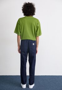 Tricou verde oversized, cu mâneci scurte, detalii cusute, asortat cu pantaloni cargo bleumarin cu buzunare. Adidași albi vizibili.