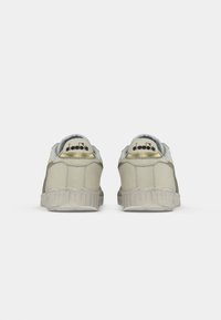 Beige sneakers with a textured surface, contrasting green accents, gold detailing on the heel, and a rubber outsole.