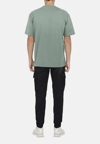 Mint green oversized t-shirt with short sleeves, paired with black cargo pants featuring side pockets and elastic cuffs, worn with white sneakers.